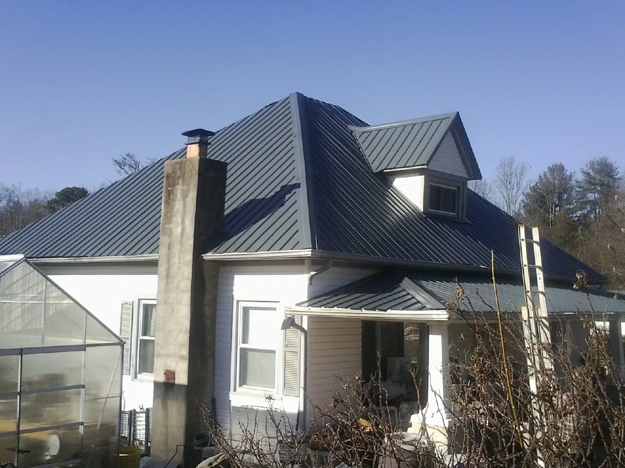 Dark blue standing seam metal roof on a white farmhouse with dormer — Slate & Tile Roof Repair by Roofing Brothers in West Augusta