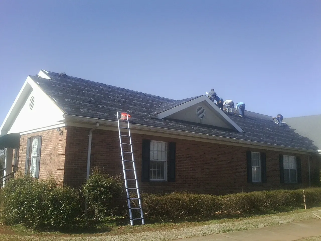Crew tearing shingles off a brick ranch roof with a ladder set — Emergency Roof Repair work by our crew in West Augusta