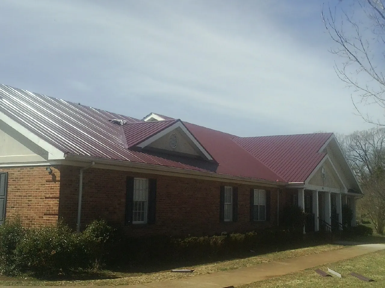 Red metal roof with gabled entries on a long brick building, from a Hail Damage Roof Repair job in West Augusta