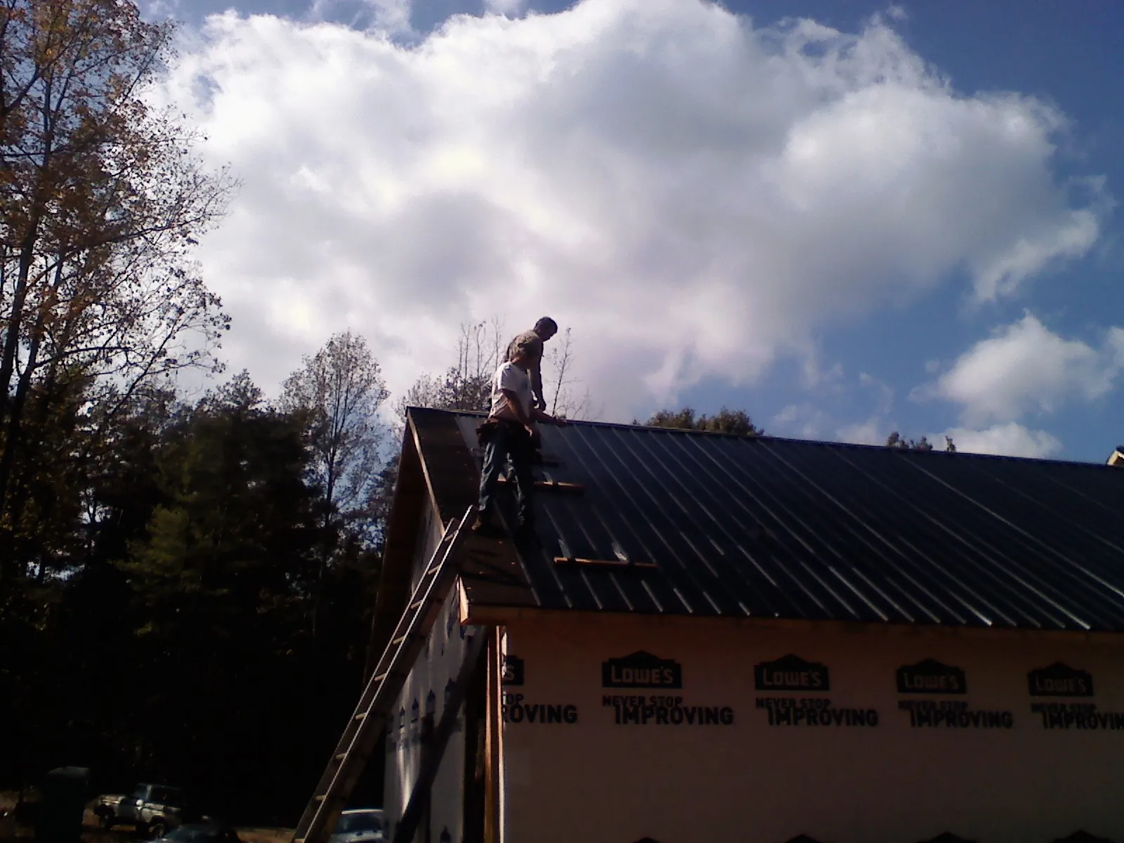 Roofer fastening dark metal panels high against a cloudy sky, from a Roof Inspection job in West Augusta